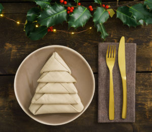 Christmas place setting with golden silverware, holly, fairy lights and a napkin folded as a Christmas tree